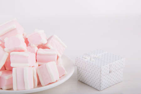 Soft pink and white marshmallow on plate with white gift box on white background. Pastel close-up sweets.の写真素材