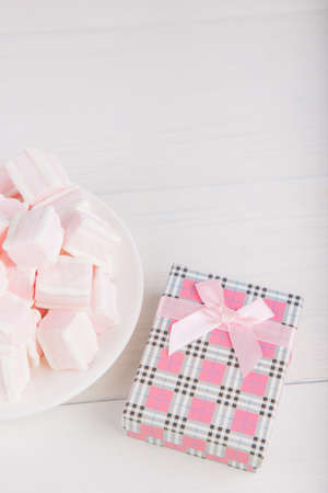 Soft pink and white marshmallow on plate with pink gift box on white background. Pastel close-up sweets.の写真素材