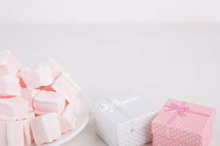 Soft pink and white marshmallow on plate with two gift boxes on white background. Pastel close-up sweets.の写真素材