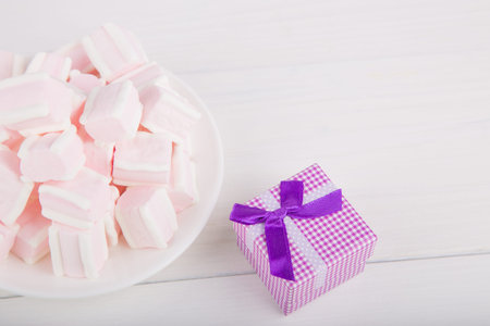 Soft pink and white marshmallow on plate with purple gift box on white background. Pastel close-up sweets.の写真素材