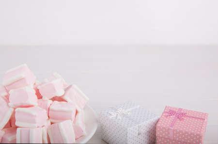 Soft pink and white marshmallow on plate with two gift boxes on white background. Pastel close-up sweets.の写真素材