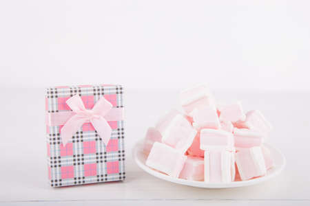 Soft pink and white marshmallow on plate with pink gift box on white background. Pastel close-up sweets.の写真素材