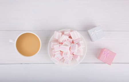 Soft pink and white marshmallow on plate with two gift boxes and cup of coffee with milk on white background. Pastel close-up sweets.の写真素材