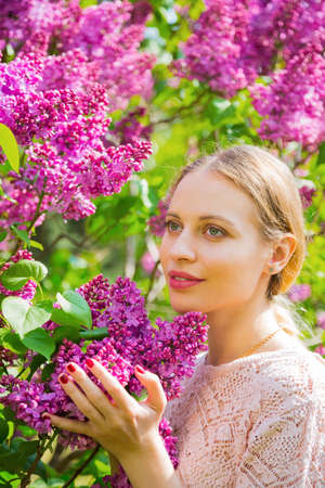 Close-up portrait of beautiful blond young woman standing between blooming lilac bushes in spring garden.の写真素材