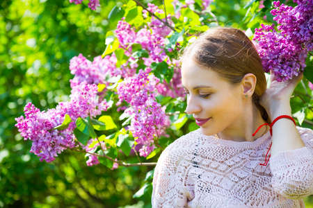 Close-up portrait of beautiful blond young woman standing between blooming lilac bushes in spring garden.の写真素材