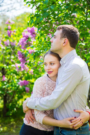 Happy young romantic couple standing between lilac bushes in spring garden.の写真素材