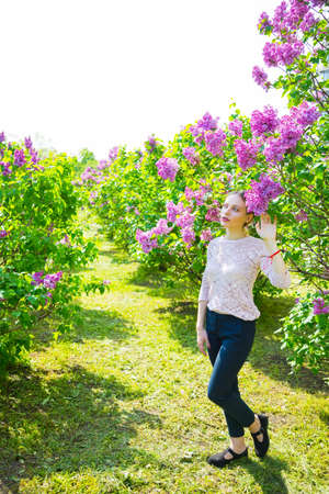 Beautiful blond young woman standing between blooming lilac bushes in spring garden.の写真素材