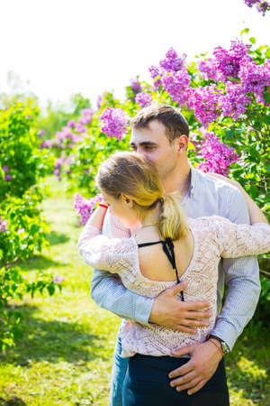 Happy young romantic couple standing between lilac bushes in spring garden.の写真素材