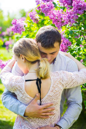 Happy young romantic couple standing between lilac bushes in spring garden.の写真素材