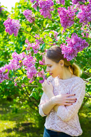 Beautiful blond young woman standing between blooming lilac bushes in spring garden.の写真素材