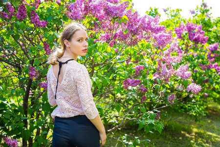 Beautiful blond young woman standing between blooming lilac bushes in spring garden.の写真素材