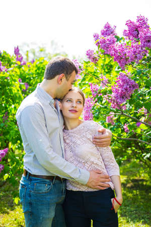 Happy young romantic couple standing between lilac bushes in spring garden.の写真素材