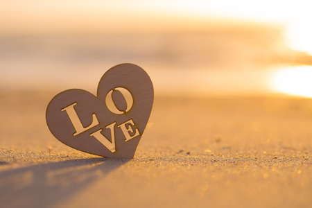 Wooden heart with inscription Love on sand on seaside at dawn. Vintage romantic image.の写真素材
