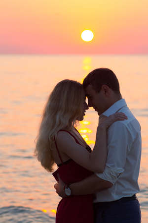 Beautiful young romantic couple on seaside in rays of rising sun. Two happy lovers at golden sunrise. Warm colors.の写真素材