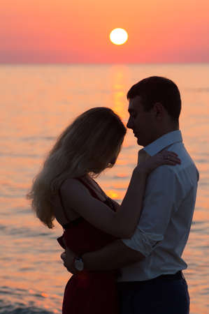 Beautiful young romantic couple on seaside in rays of rising sun. Two lovers at golden sunrise. Warm colors.の写真素材