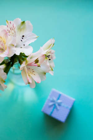 Beautiful tender bouquet of white Alstroemeria with blue gift box on pastel green background. Spring composition. Springtime. Mother`s day card.の写真素材