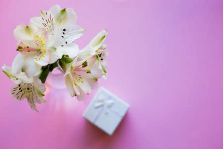 Beautiful tender bouquet of white Alstroemeria with white gift box on pink background. Spring composition. Springtime. Mother`s day card.の写真素材