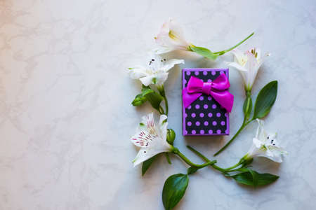 Purple spotted gift box surrounded with alstroemeria flowers on marble surface. Spring composition. Springtime. Mother`s day card.の写真素材