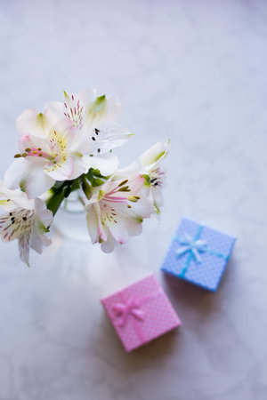 Beautiful tender bouquet of white Alstroemeria with two gift boxes on marble table. Spring composition. Springtime. Mother`s day card.の写真素材