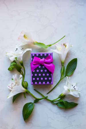 Purple spotted gift box surrounded with alstroemeria flowers on marble surface. Spring composition. Springtime. Mother`s day card.の写真素材