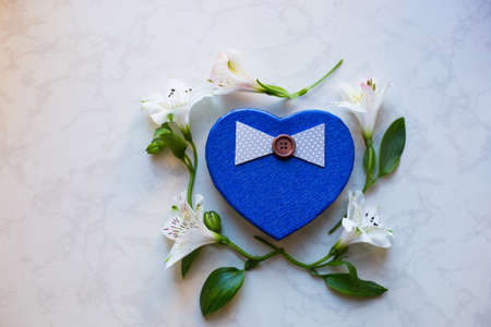 Blue gift box in shape of heart surrounded with alstroemeria flowers on marble surface. Spring composition. Springtime. Mother`s day card.の写真素材