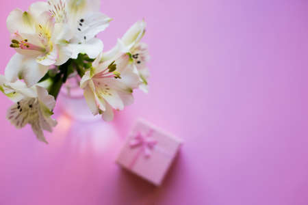 Beautiful tender bouquet of white Alstroemeria with pink gift box on pink background. Spring composition. Springtime. Mother`s day card.の写真素材
