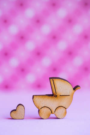 Wooden icon of baby buggy and little heart on pink spotted background. Sign of baby carriage. Symbol of childbirth.の写真素材