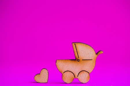 Wooden icon of baby buggy and little heart on crimson background. Sign of baby carriage. Symbol of childbirth.の写真素材