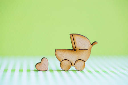 Wooden icon of baby buggy and little heart on green background. Sign of baby carriage. Symbol of childbirth.の写真素材