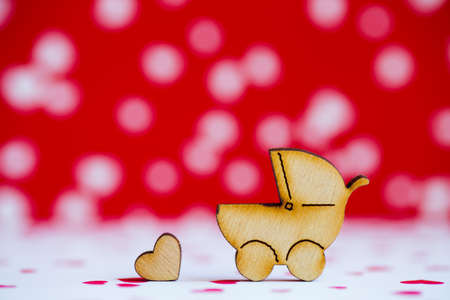 Wooden icon of baby buggy and little heart on red and white spotted background. Sign of baby carriage. Symbol of childbirth.の写真素材