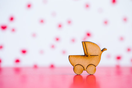 Wooden icon of baby buggy on pink and white background. Sign of baby carriage. Concept of...
