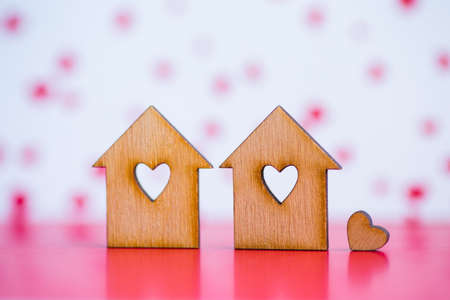 Two wooden houses with hole in form of heart with little heart on pink and white background.の写真素材