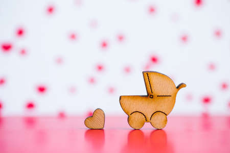 Wooden icon of baby buggy and little heart on pink and white background. Sign of baby carriage. Symbol of childbirth.の写真素材
