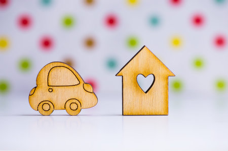 Wooden house with hole in form of heart with wooden car icon on colorful spotted background. Concept of moving or traveling.の写真素材
