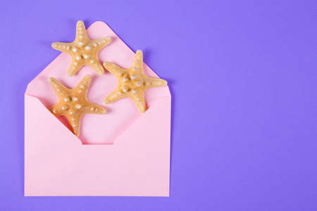 Pink envelope with three starfishes on colored purple background. Summer minimalistic card. Top view. Sea flat lay.の写真素材