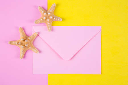Pink envelope with two starfishes on colored pink and yellow backgrounds with negative space. Minimalistic colorful summer background. Top view. Flat lay in marine style.の写真素材