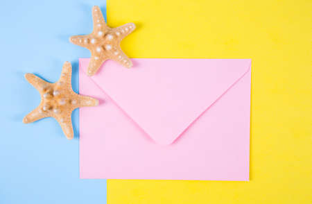 Pink envelope with two starfishes on colored blue and yellow backgrounds with negative space. Minimalistic colorful summer background. Top view. Flat lay in marine style.の写真素材