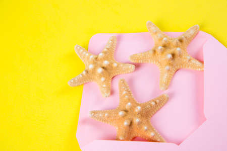 Pink envelope with three starfishes on colored yellow background. Summer minimalistic card. Top view. Sea flat lay.の写真素材