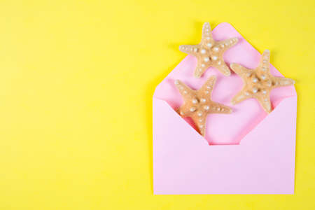 Pink envelope with three starfishes on colored yellow background. Summer minimalistic card. Top view. Sea flat lay.の写真素材