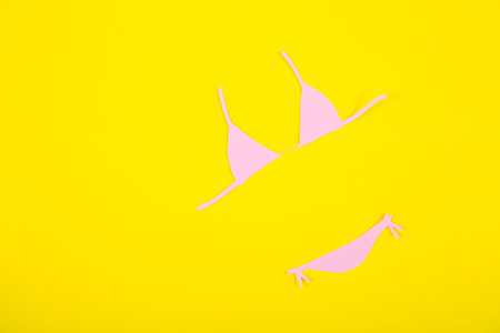 Pink paper bikini swimsuit on yellow background. Minimalistic summer colorful flat lay with negative space. Beach concept.の写真素材