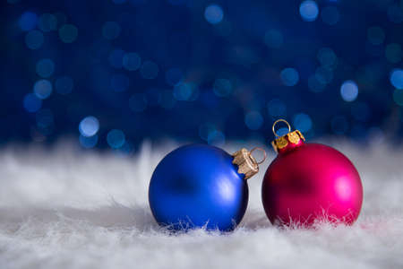 Two Christmas balls on white fur with garland lights on blue bokeh background. New year card with empty space. Xmas festive decoration.の写真素材