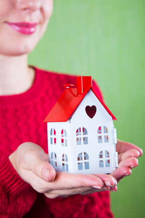 Young female hands holding toy house with hole in form of heart on green backgroundの写真素材