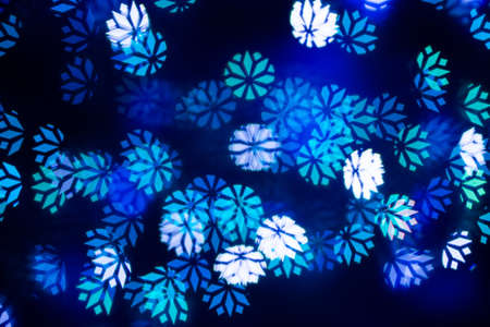 Blue festive bokeh in shape of snowflakes on dark background.の写真素材