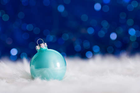 Pastel blue Christmas ball on white fur with garland lights on blue bokeh background. New year card with empty space. Xmas festive decoration.の写真素材