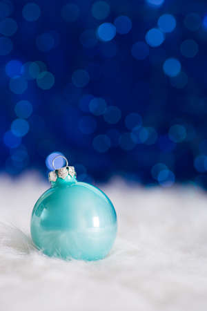 Pastel blue Christmas ball on white fur with garland lights on blue bokeh background. New year card with empty space. Xmas festive decoration.の写真素材