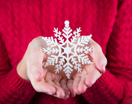 Young female hands holding white snowflake on background of red knitted sweater. New year card. Xmas banner.の写真素材