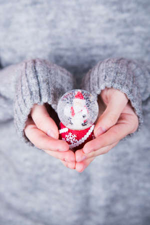 Beautiful Christmas glass snowball in female hands on background of gray knitted sweater. New year card. Xmas banner.の写真素材