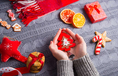 Female hands in gray knitted sweater holding little wooden Christmas tree with decor on background. New Year decoration with dried citrus fruits, cookies, gifts and gingerbread. の写真素材