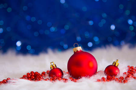Red Christmas balls and beads on white fur with garland lights on blue bokeh background.  New year card with empty space. Xmas festive decoration.の写真素材