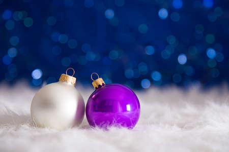 Two Christmas balls on white fur with garland lights on blue bokeh background. New year card with empty space. Xmas festive decoration.の写真素材